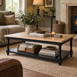 A rectangular coffee table with a light natural wood top and a black metal frame with turned legs, styled in a cozy living room with books, a candle, and baskets on a woven rug.