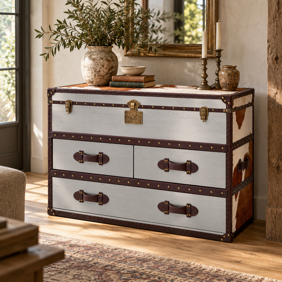 Westbury House Brown and White Cowhide Cabinet styled in a living room with an olive branch vase, candlesticks and books