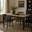 Natural wood dining table with black turned legs, styled with black dining chairs, a ceramic vase of greenery and pears in a warm, rustic dining room.