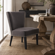 A dark grey upholstered accent chair with black legs and silver nailhead trim, positioned in a dining room next to a rustic wooden table.