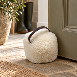 White sheepskin doorstop with leather handle holding open a sage green door on a stone hallway floor