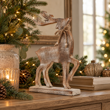 Whitewashed wooden reindeer with twine bow on a wooden sideboard with books, candles and pine greenery