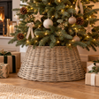 Wicker tree skirt around the base of a decorated Christmas tree, with wrapped presents on a wooden floor