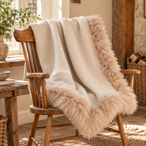 Woven Beige Wool Blanket With Sheepskin Trim draped over a wooden Windsor chair by a stone fireplace with a log basket and olive branches