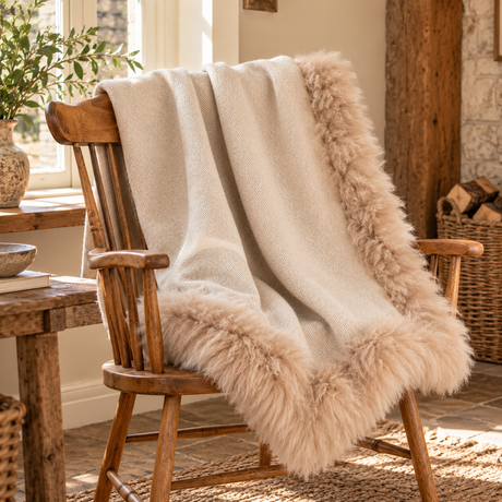 Woven Beige Wool Blanket With Sheepskin Trim draped over a wooden Windsor chair by a stone fireplace with a log basket and olive branches
