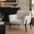 A light beige textured fabric armchair with black tapered legs, styled in a modern living room setting next to a black sideboard and a round black coffee table.