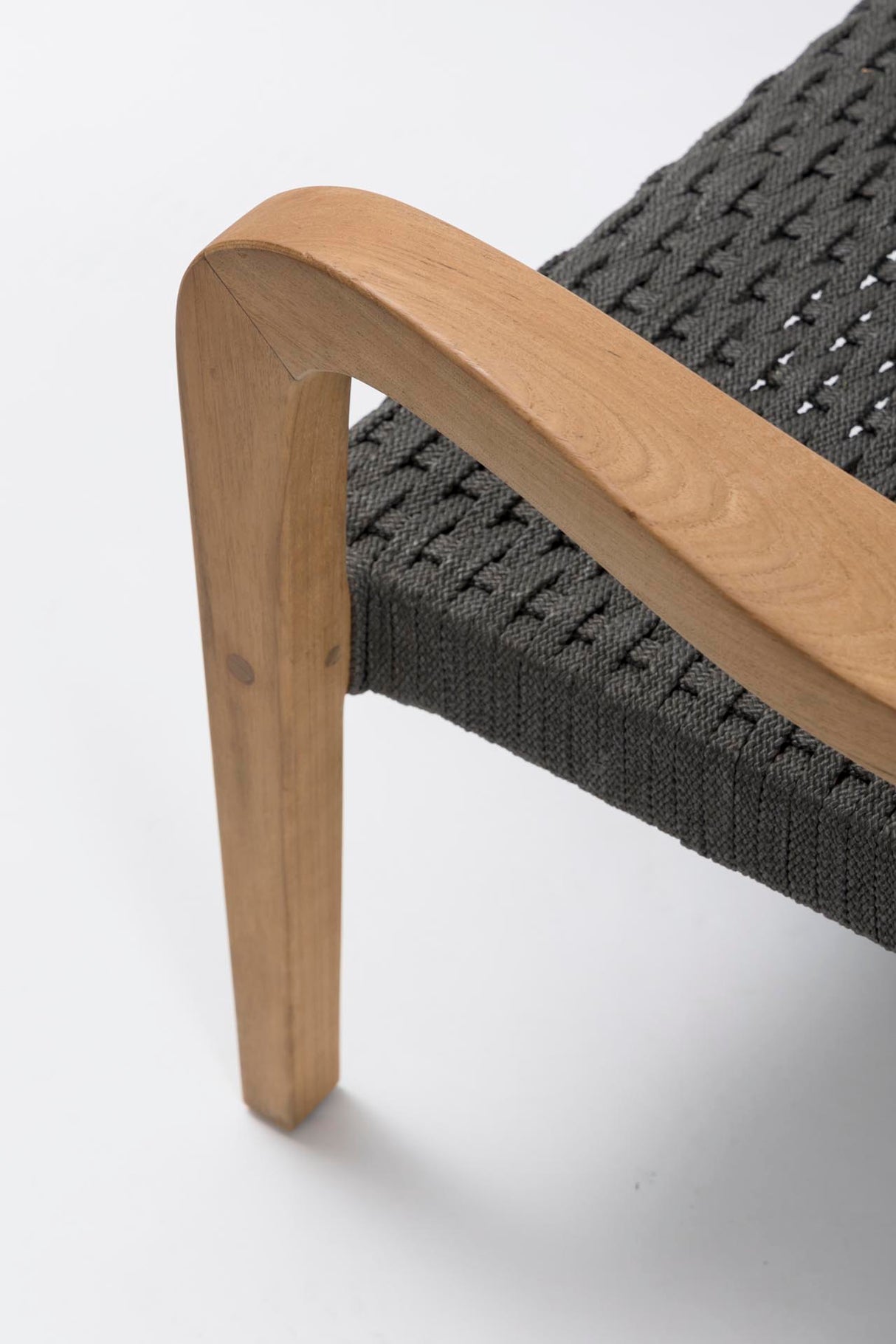 Close-up of a modern lounge chair featuring a curved natural wood armrest and leg, paired with a dark grey woven rope seat on a white background.
