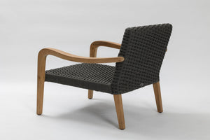 A modern outdoor lounge chair with a black woven rope seat and backrest, supported by curved light brown wooden arms and legs, shown from a three-quarters angle on a light grey studio background.
