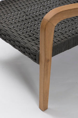 Close-up of a woven dark grey outdoor chair or bench with a curved natural wood armrest and leg on a light grey studio background.