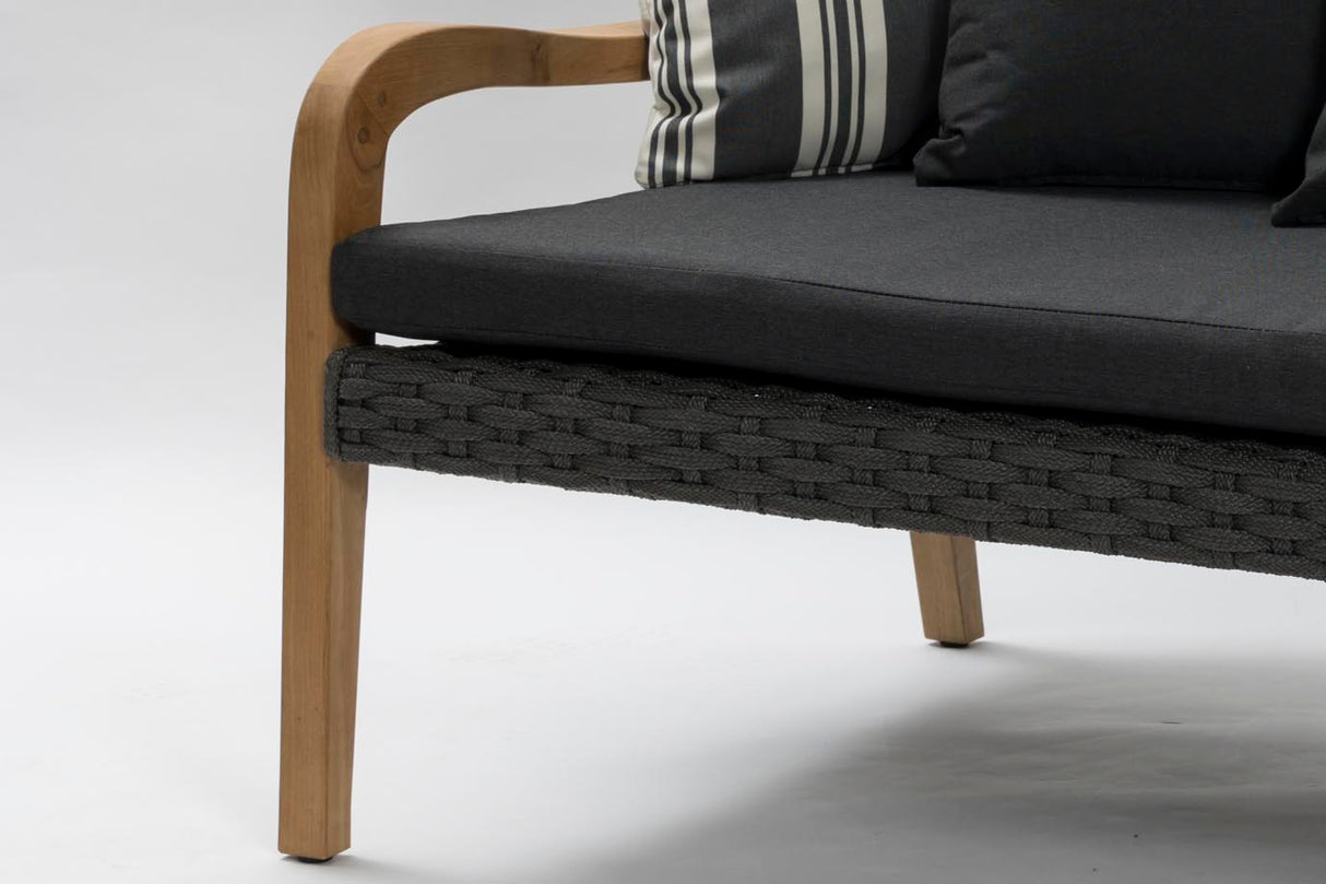 Close-up of a modern outdoor sofa with a dark gray cushion, a light natural wood frame, and a dark woven seat strap, with a striped accent pillow visible.