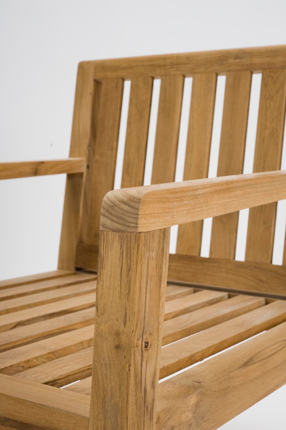 Close-up of a wooden outdoor chair showing the armrest, slatted backrest, and seat slats in a warm natural wood finish against a plain light background.