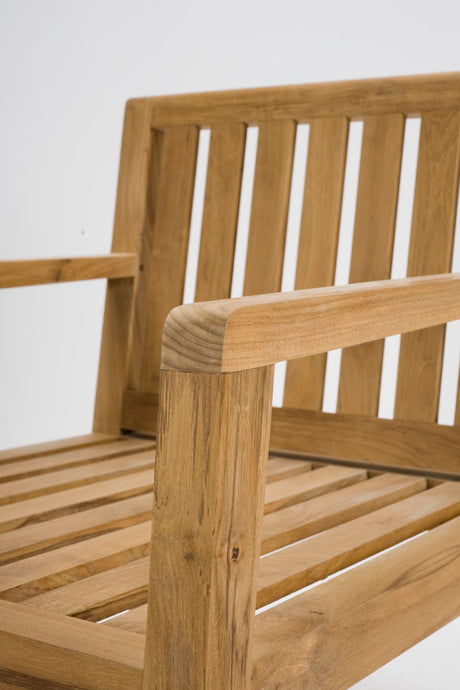 Close-up of a wooden outdoor chair showing the armrest, slatted backrest, and seat slats in a warm natural wood finish against a plain light background.