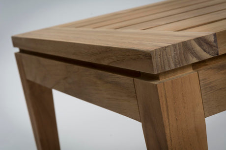 Close-up of a wooden slatted table corner showing the tabletop, leg joint, and natural wood grain on a light grey background.