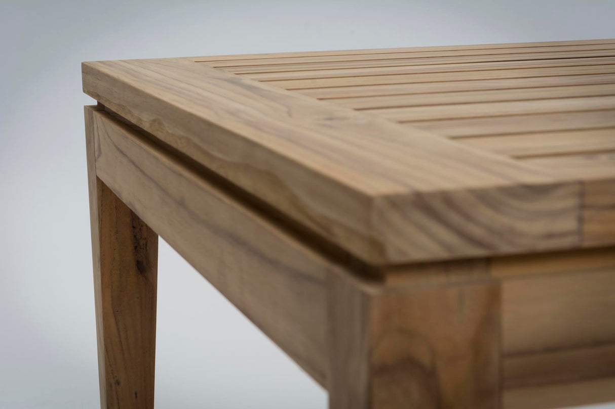 Close-up of a light natural wood slatted table corner showing the tabletop slats, thick wood edge, and leg on a light grey background.