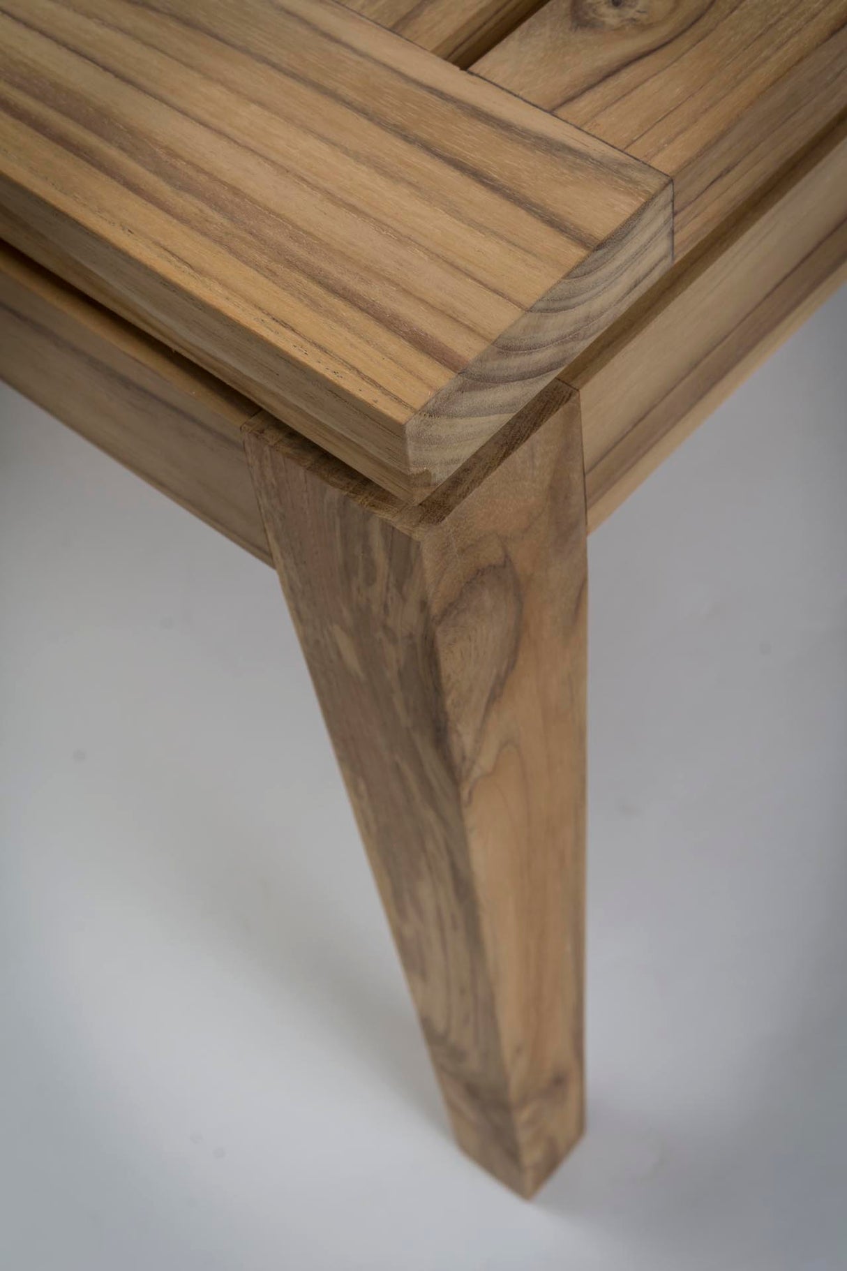 Close-up of a wooden table corner showing the tabletop and front leg with visible wood grain and a light grey background.