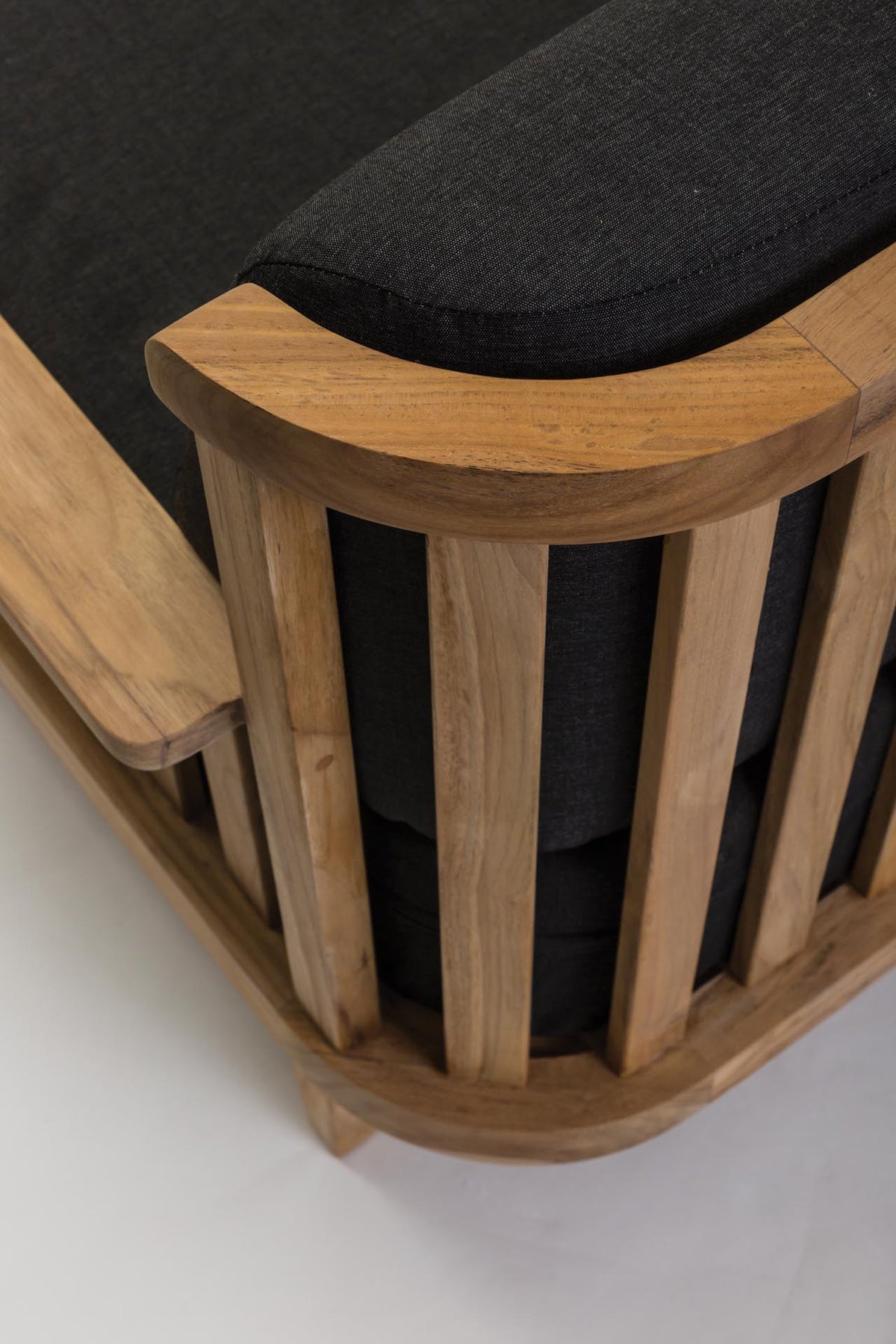 Close-up of a wooden armchair corner with a curved natural oak frame and dark charcoal gray fabric cushions.