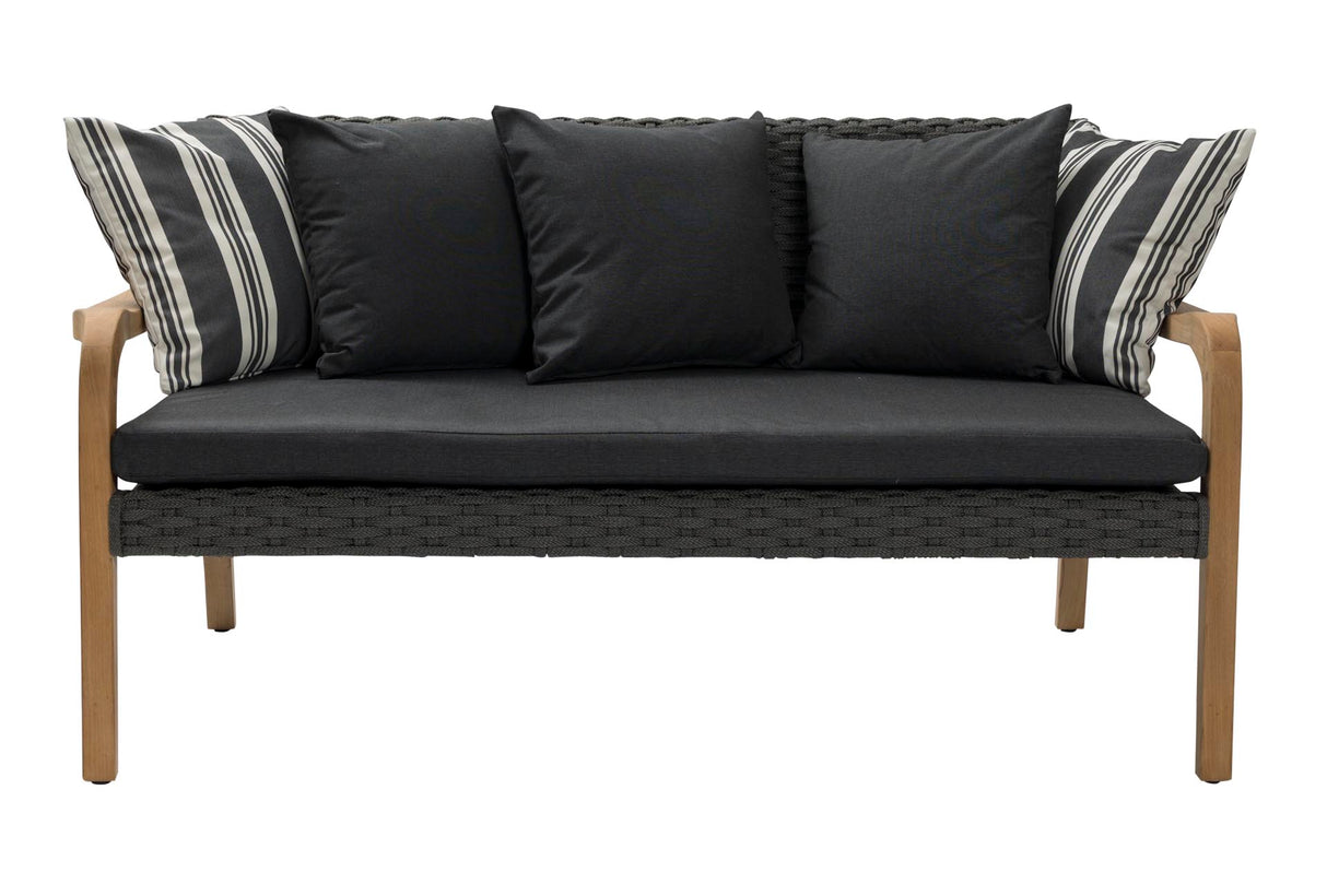 A modern outdoor loveseat with a dark gray woven wicker frame, black seat and back cushions, and light brown wooden legs. It features four throw pillows, including two black pillows and two striped black-and-white pillows, shown against a plain white background.