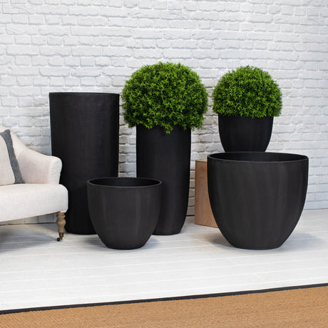 Set of black planters with green plants against a white brick wall.