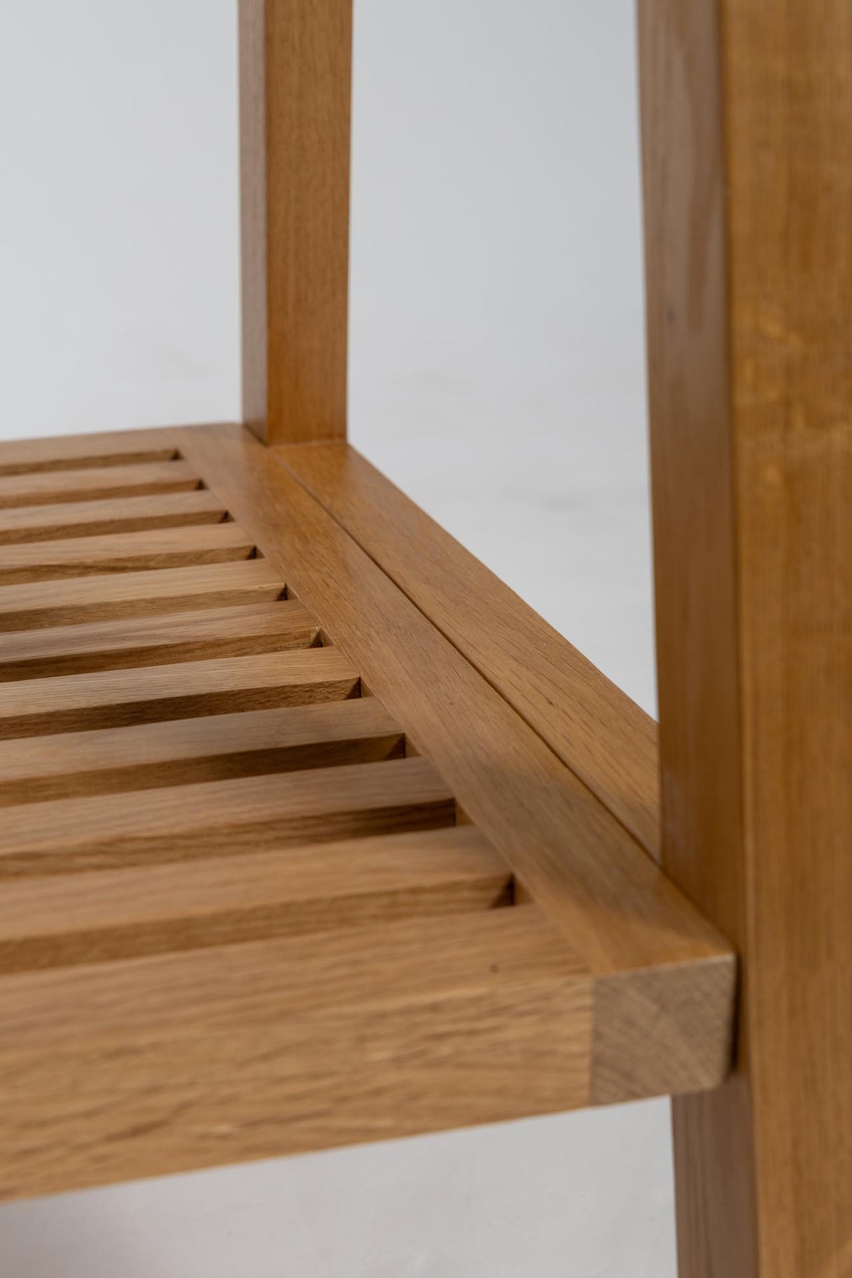 Close-up of a wooden slatted shelf or stool leg with a warm medium-brown wood finish and visible grain, photographed against a plain light background.