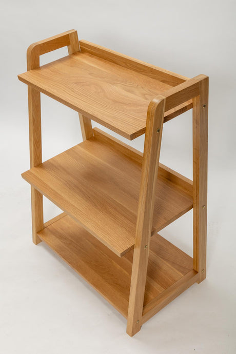 A three-tier wooden shelf unit with a warm natural oak finish, featuring a top handle and open side compartments, shown on a light grey background.