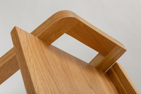 Close-up of a light oak wood chair showing the grain, curved armrest, and clean minimalist design against a neutral light gray background.